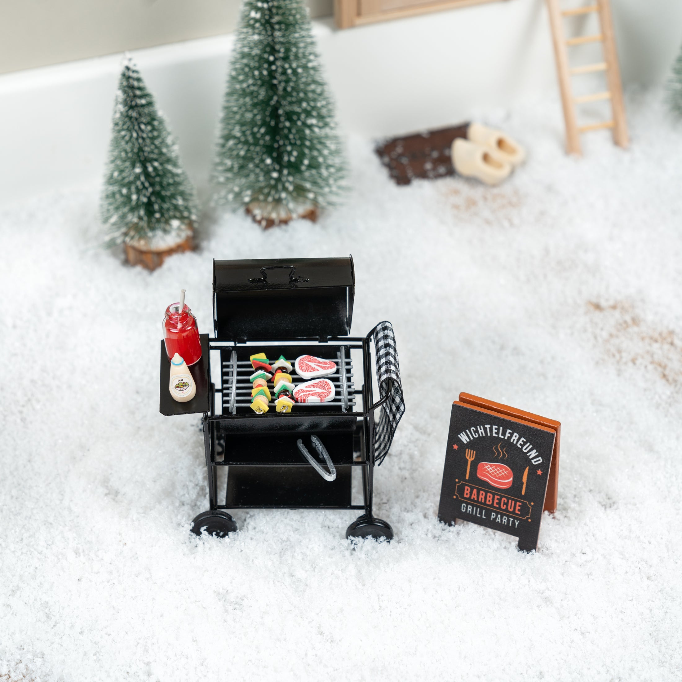 Wichtelgrill-Set mit Miniatur-Holzkohlegrill, Grillzubehör und Barbecue-Schild in einem verschneiten Wichteldorf. Perfektes Zubehör für Wichtel-Fans.